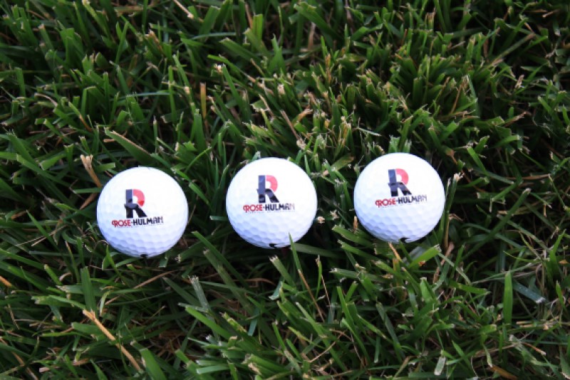 Golf Balls lying in the grass with Varsity R Club logo on the golf balls.